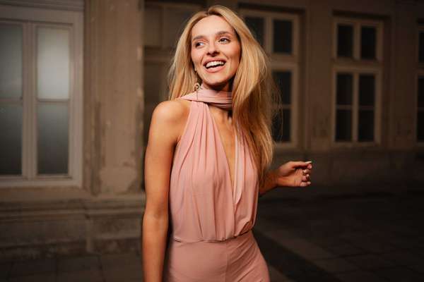 A radiant woman wearing a chic pink dress smiles joyfully during an evening stroll.