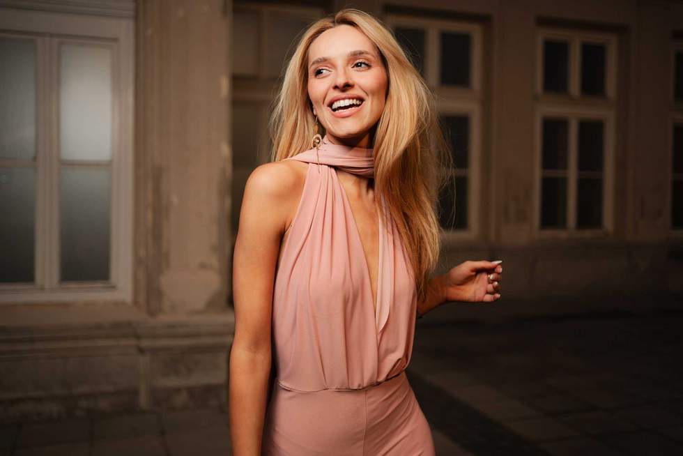 A radiant woman wearing a chic pink dress smiles joyfully during an evening stroll.