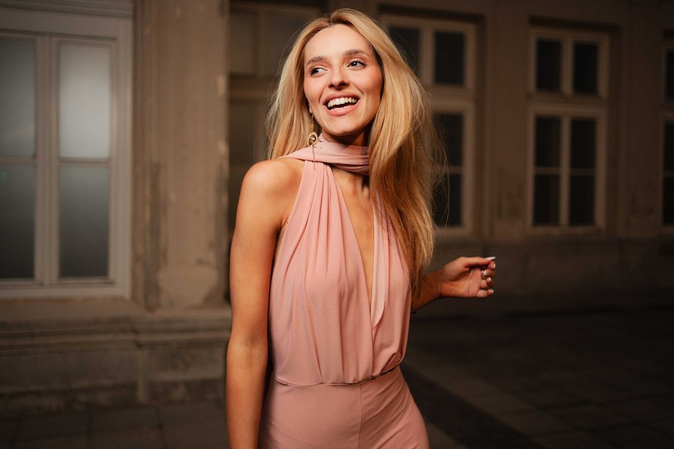 A radiant woman wearing a chic pink dress smiles joyfully during an evening stroll.