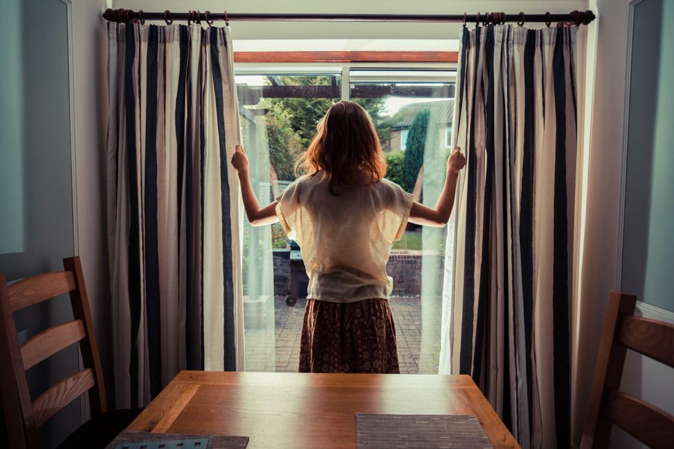 A young woman is opening the curtains at sunrise