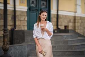A young woman with a smartphone and coffee in a cup in an urban area of the city, a girl communicates on a mobile phone on the street in summer. High quality photo