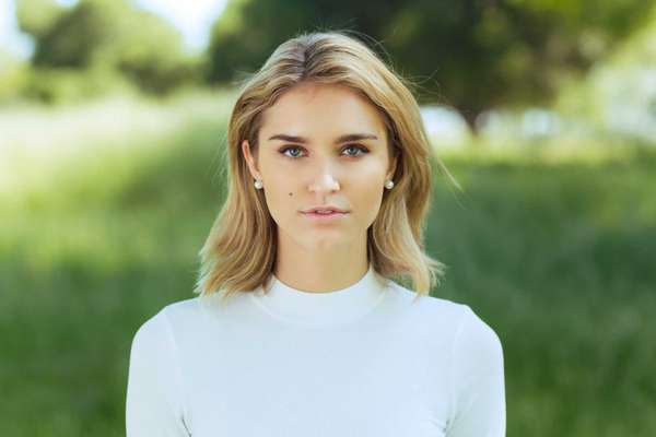 Attractive young blonde Caucasian woman in tight white top and denim posing outside among long grass and trees