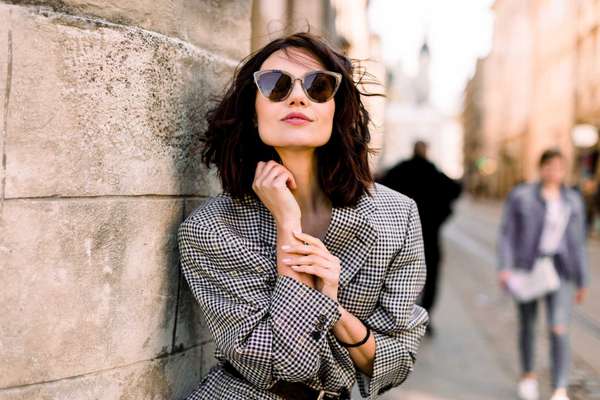 Beautiful brunette young woman wearing jacket and black sunglasses walking on the street, posing near the old building in ancient city