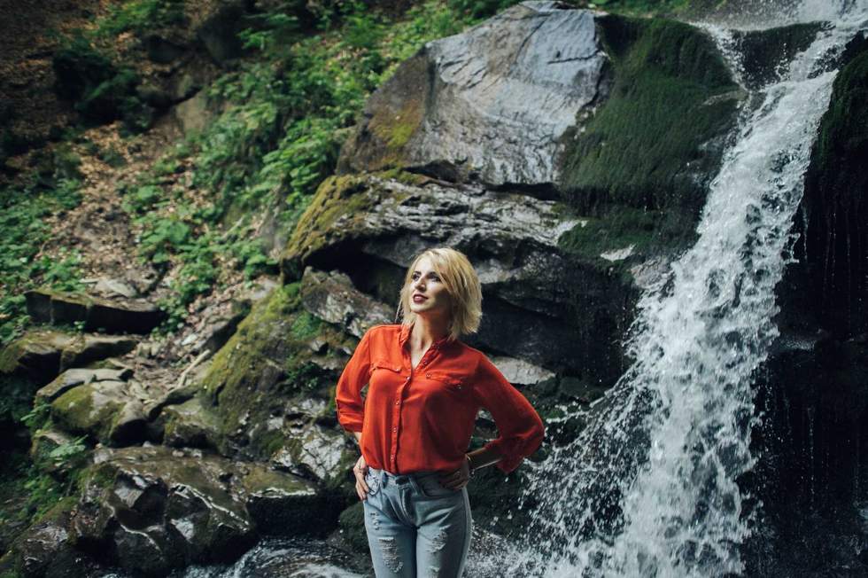 beautiful woman posing near waterfall on forest background.