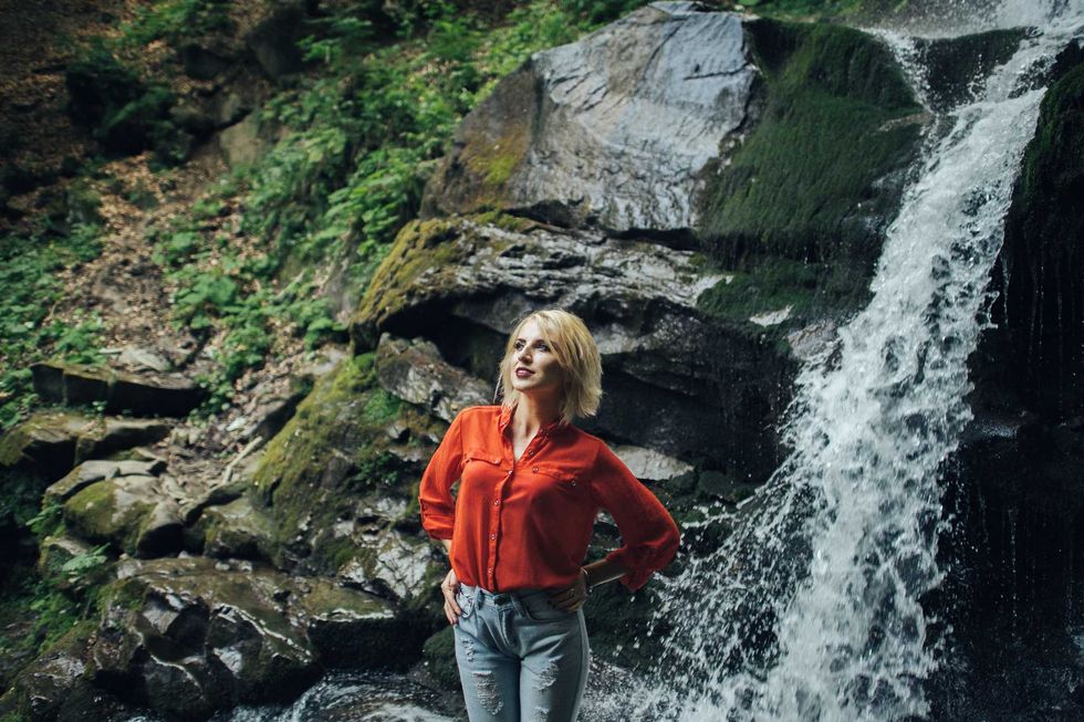 beautiful woman posing near waterfall on forest background.
