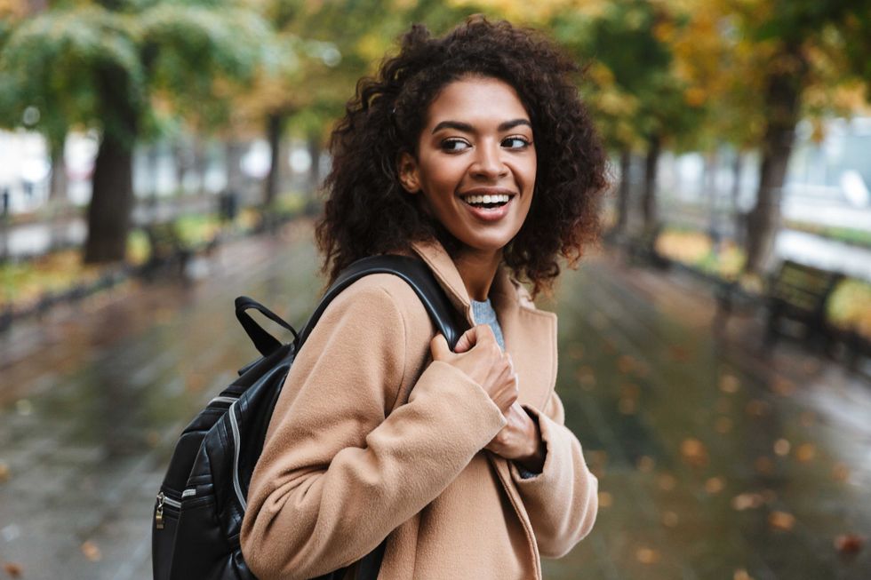 Beautiful young african woman wearing coat walking outdoors at the park, carrying backpack
