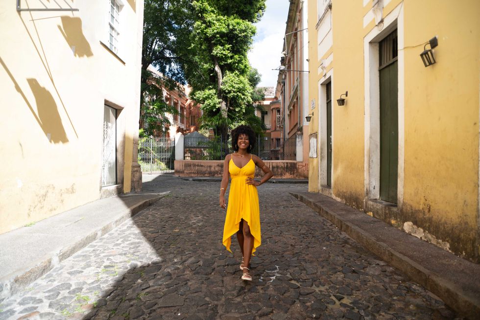 Beautiful young black woman walking on the cobblestone streets wearing yellow clothes, with afro hair, smiling and happy. Confident person on a trip