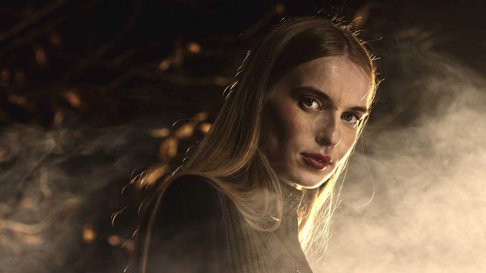 Blonde fashion model posing dramatically in a dark, smoky environment, enhancing the mysterious atmosphere with an elegant expression and captivating style