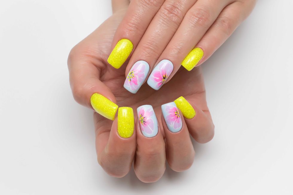 Bright yellow and blue summer manicure with painted flowers on square long nails with sparkles. Sunny manicure. Pink flowers. Close-up on a white background.