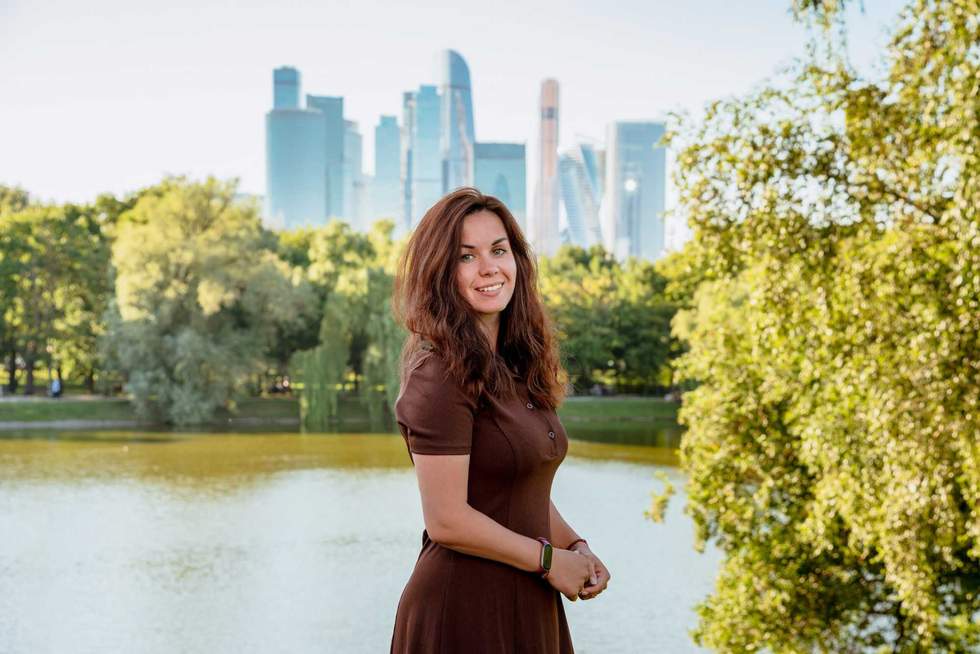 Caucasian young woman in a green park by a pond with skyscrapers in the background in Moscow