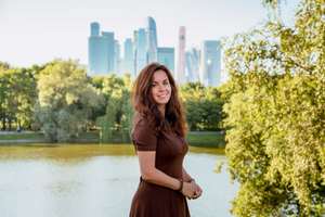 Caucasian young woman in a green park by a pond with skyscrapers in the background in Moscow