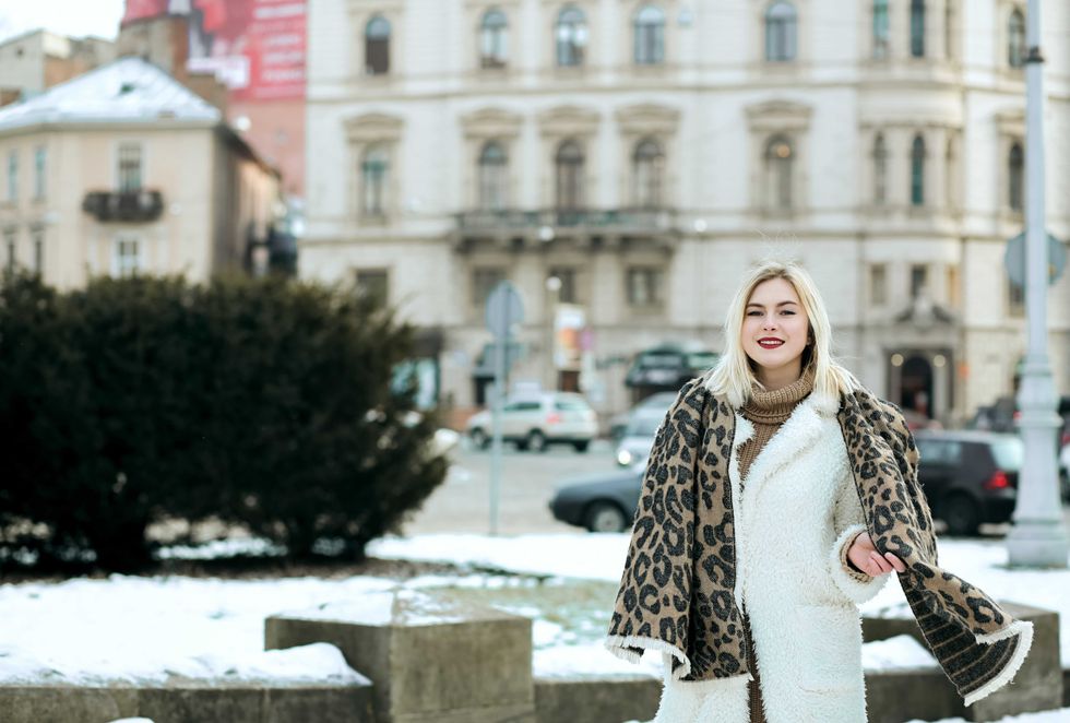 Cheerful blonde woman wears winter coat and knit scarf walking at the city. Space for text