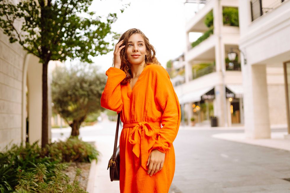 Cheerful tourist in a bright dress walks along a beautiful street. A young woman enjoys the weather outdoors. The concept of walking, vacation, travel. Active lifestyle.
