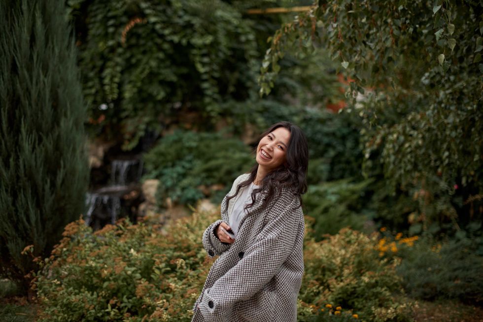 Close-up portrait of beautiful pretty asian kazakh brunette woman in plaid coat with charming smile walking along outdoors in park. Happy face. Autumn season. Cozy.