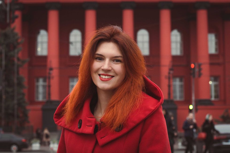 Close up young smiling woman in red coat on street portrait picture. Closeup front view photography with public building on background. High quality photo for ads, travel blog, magazine, article