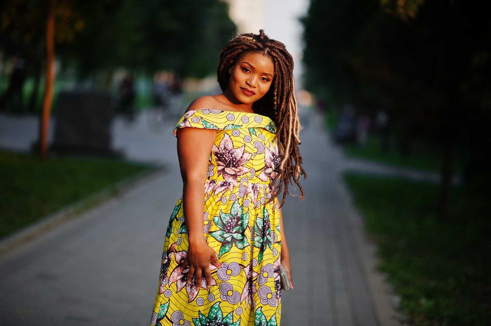 Cute small height african american girl with dreadlocks, wear at coloured yellow dress, posed at sunset.