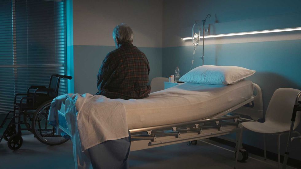 Depressed senior man sitting on the hospital bed alone at night, he feels lonely and abandoned