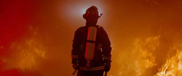 Dramatic silhouette of American firefighter in full gear exploring the huge fire zone