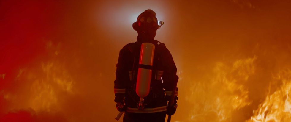 Dramatic silhouette of American firefighter in full gear exploring the huge fire zone