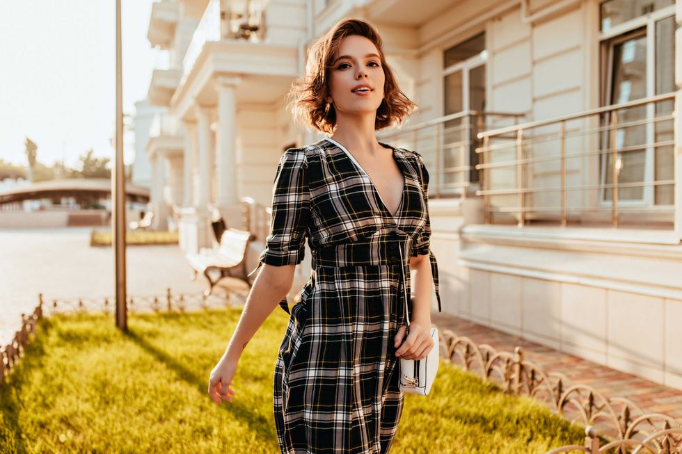 Enchanting caucasian lady in elegant dress posing in city. Glad white woman with wavy hair walking down the street in sunny day.