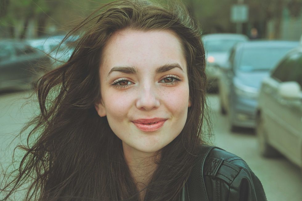 Happy girl posing outside in the street with parked cars on background looking at camera with windy hair