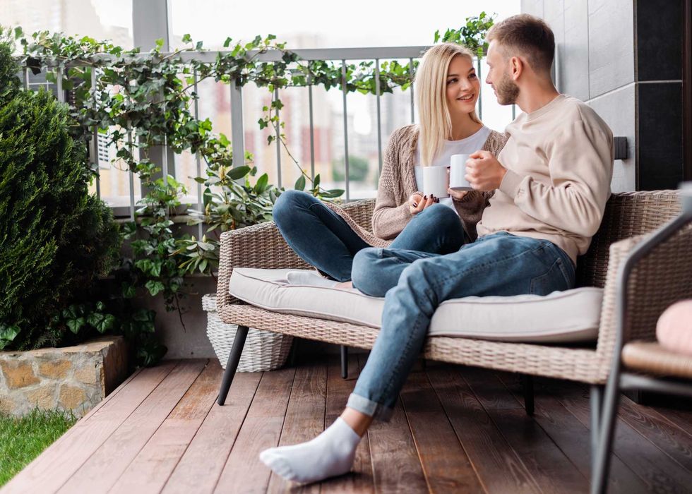 happy woman and man looking at each other and holding cups while sitting on outdoor sofa
