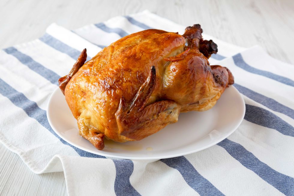 Homemade tasty rotisserie chicken on white plate, side view. Close-up.