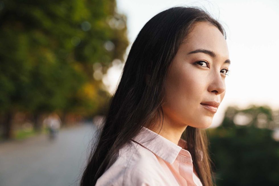 Image of pleased asian beautiful girl looking aside while walking in summer park