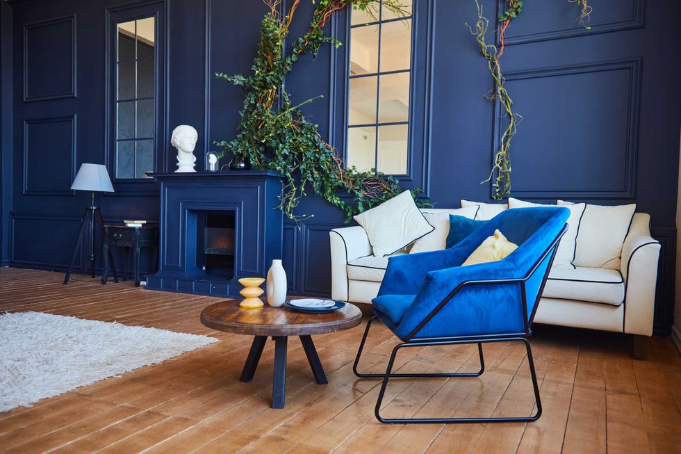 Modern interior with a fireplace, a spacious living room with blue walls and wooden floors, a blue armchair in the foreground and a white sofa against the wall. The concept of art Nouveau style, a real photo of the interior.