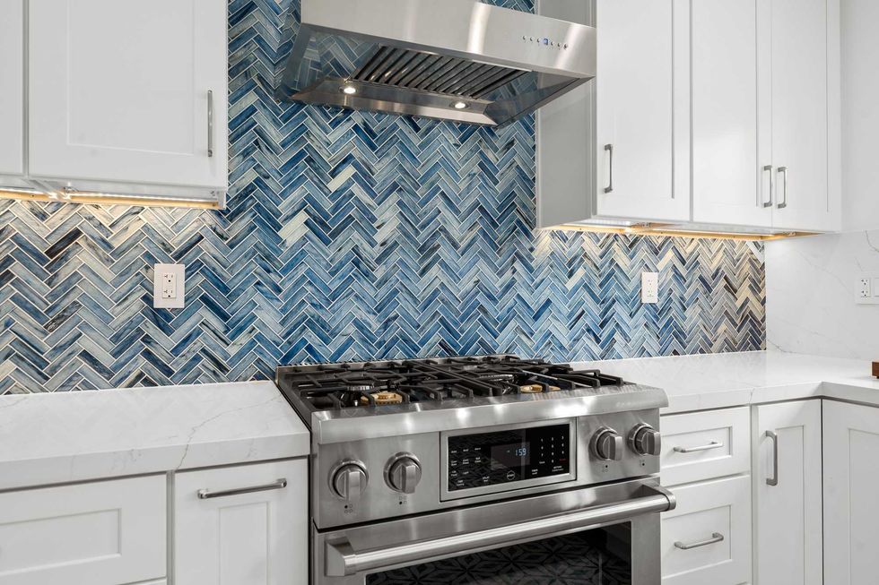 Modern white kitchen with blue tile backsplash, stainless steel appliances, and minimalist cabinetry