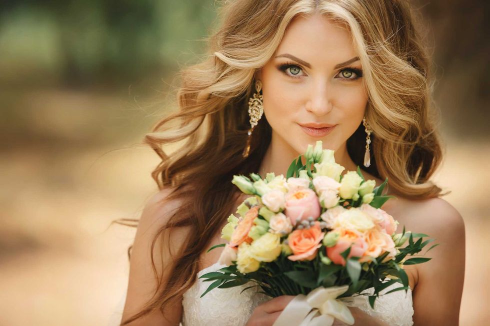 Portrait of beautiful luxury bride with roses wedding bouquet outdoors. Young woman with professional make up and hair style. Wedding day. Marriage