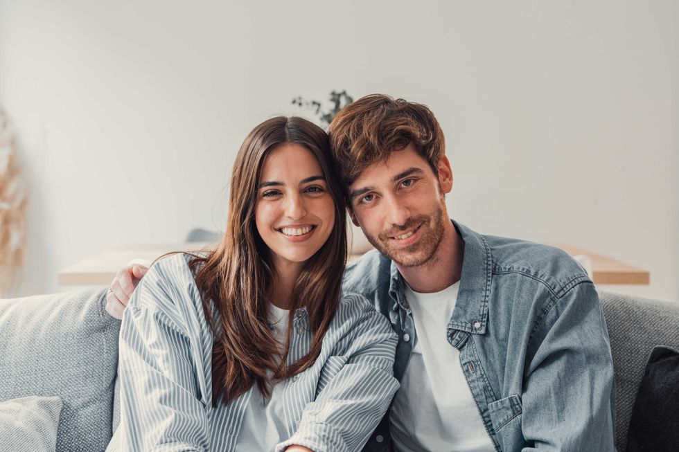 Portrait of young 20s just married couple in love posing photo shooting seated on couch in modern studio apartments, concept of capture happy moment, harmonic relationships, care and sincere feelings