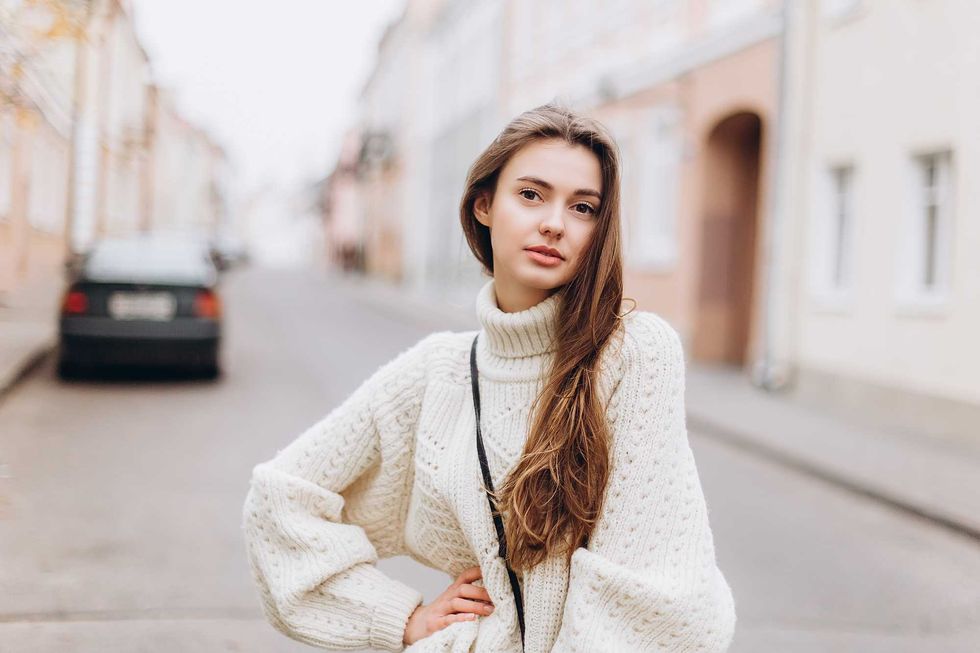 Portrait of young tender redhead young girl with healthy freckled skin wearing knitted scarf looking at camera with serious,pensive expression. Caucasian teen model with ginger hair posing outdoors