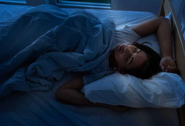 Pretty young woman sleeping restful in bed at morning with sun ray coming in room