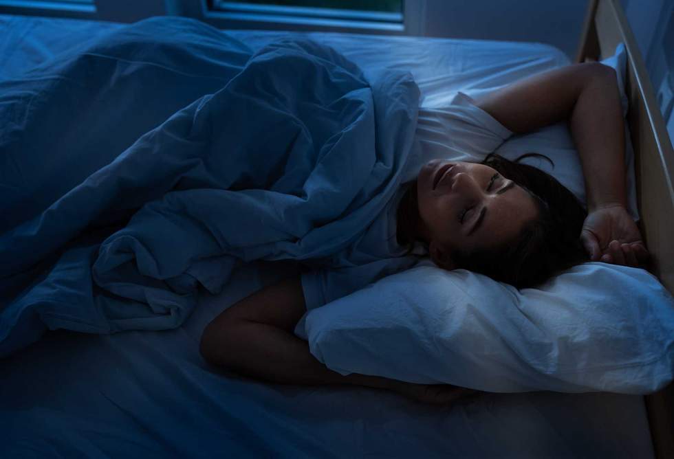 Pretty young woman sleeping restful in bed at morning with sun ray coming in room