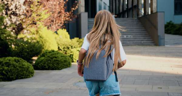 Rear view of Caucasian 11 year old girl with long hair and school bag running to school for first lesson. Education and school children life concept