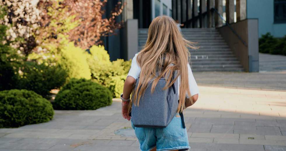 Rear view of Caucasian 11 year old girl with long hair and school bag running to school for first lesson. Education and school children life concept