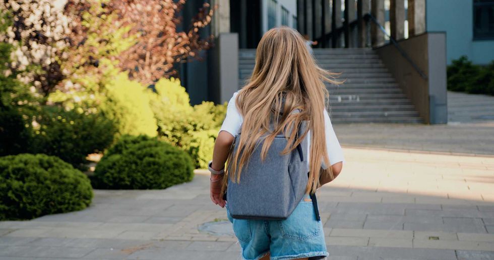 Rear view of Caucasian 11 year old girl with long hair and school bag running to school for first lesson. Education and school children life concept