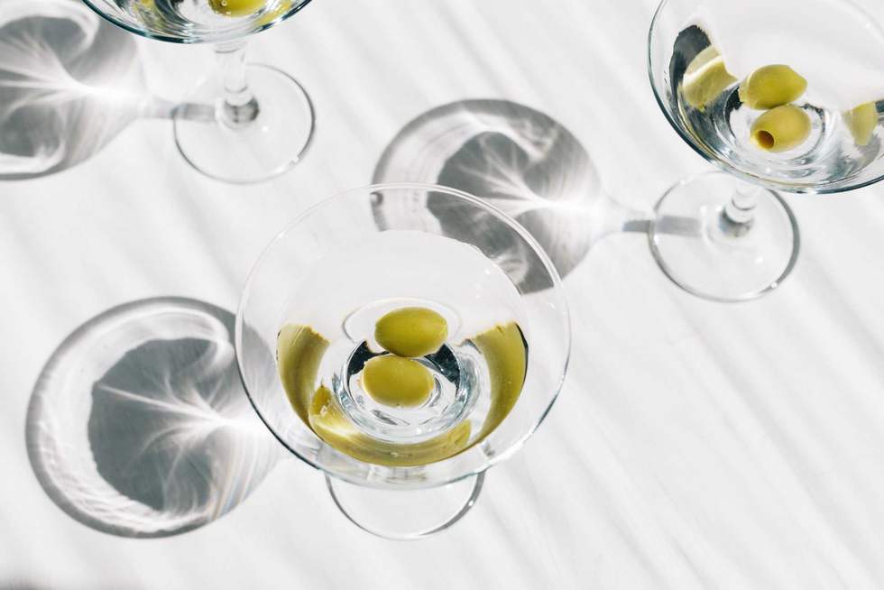 Refreshing cold dry martini cocktails with green olives on white background. Sun lighting with shadows.