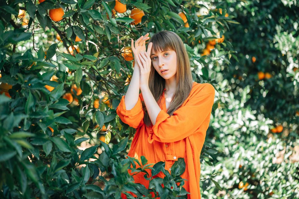 Seriously girl in orange dress is posing to camera by holding hands up together in orange garden