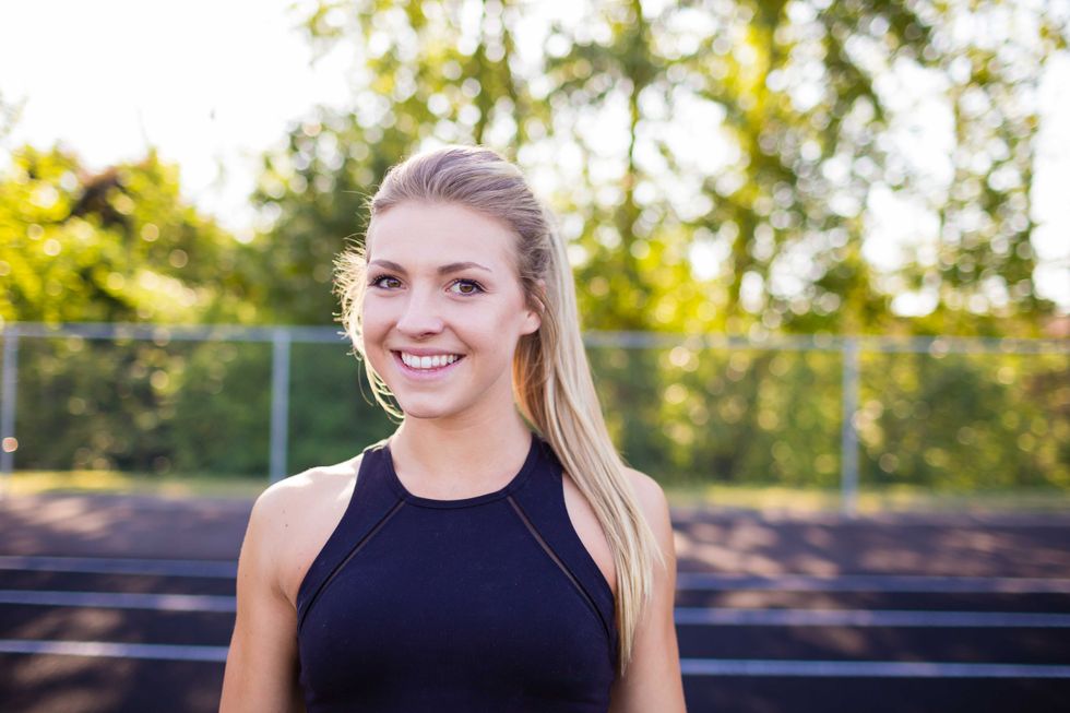 Smiling portrait of a young female athlete while working out on an outdoor track in the summer.