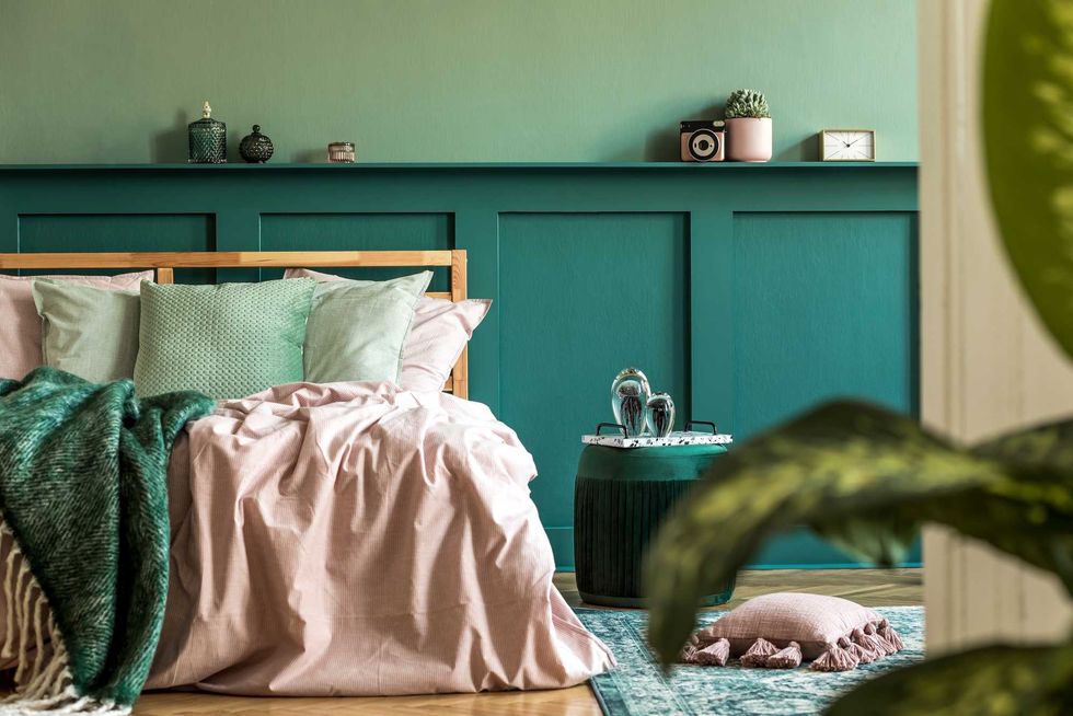 Stylish interior design of bedroom with modern furnitures, plants and elegant accessories. Shelf above the bed. Beautiful pink and green bed sheets, blankets and pillows. Modern home decor. Template.