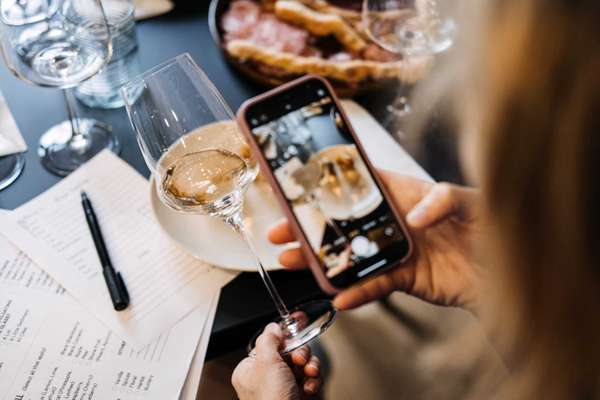 Woman photographing wine and charcuterie with smartphone at tasting table. Highlights social rituals around wine. High quality photo