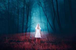 Woman standing in foggy mysterious fantasy forest with grass on the floor. The image with the effect of double exposure.