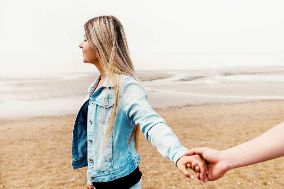 Young couple in love holding hands are walking by the beach against summer sunset. Happy young family. Travel and vacation concept.