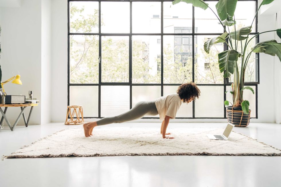Young mixed race woman exercising at home doing plank pose using online video training with laptop. Copy space. Active and healthy lifestyle concept.