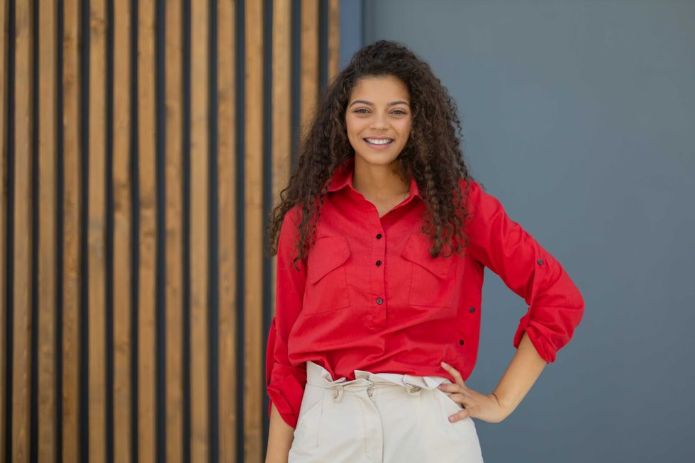 Young woman in red shirt standing against grey and wooden wall.